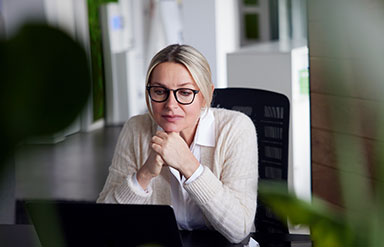 Wechseljahre – Frau schaut nachdenklich am Schreibtisch sitzend auf den Monitor