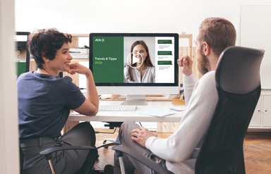 Teilnehmende eines Trends & Tipps Online-Seminars sitzen an einem Tisch und schauen sich die Präsentation an.