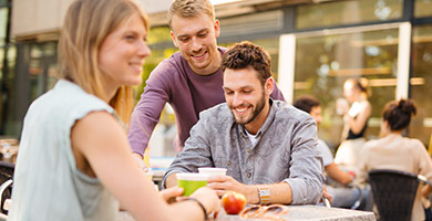 Online-Training Beschäftigung von Studenten Eine Studentin und zwei Studenten, die sich an einem Tisch in der Pause aufhalten.