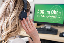 AOK im Ohr – der Arbeitgeberpodcast Eine Frau sitzt mit Kopfhörern vor einem Bildschirm mit der Schrift AOK im Ohr – der Arbeitgeberpodcast