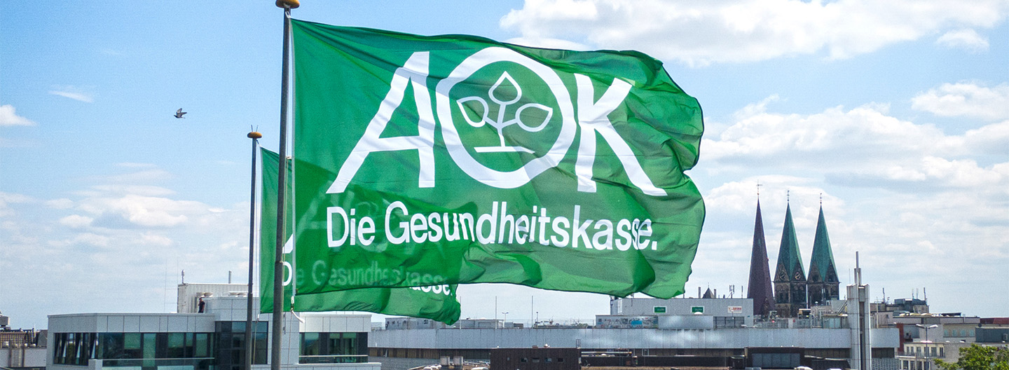 Stadtkulisse mit zwei großen AOK Die Gesundheitskasse Flaggen