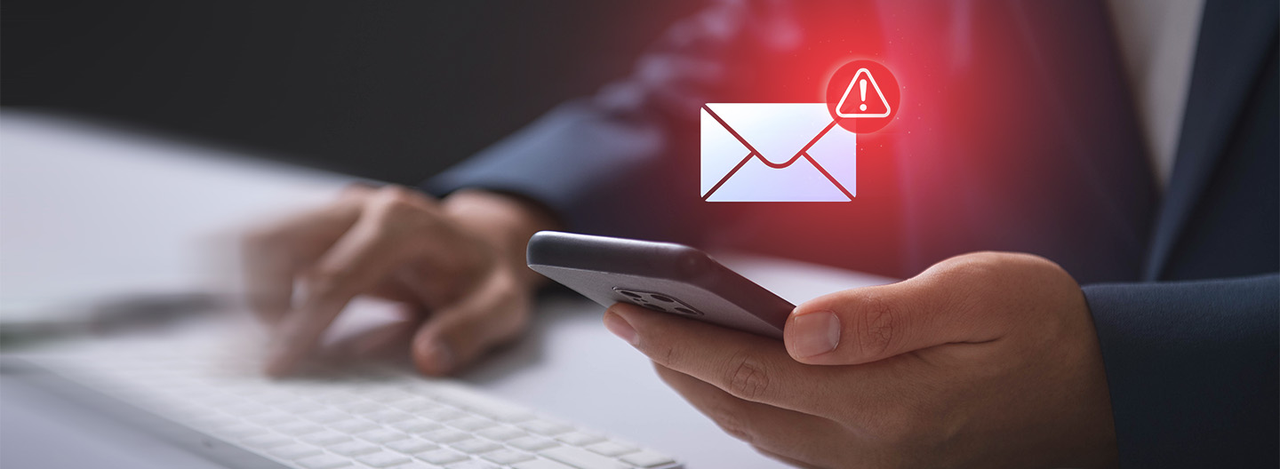 Phishing-Mails: Eine Hand hält ein Mobiltelefon, über dem ein Brief-Icon mit einem roten Ausrufezeichen sichtbar ist.