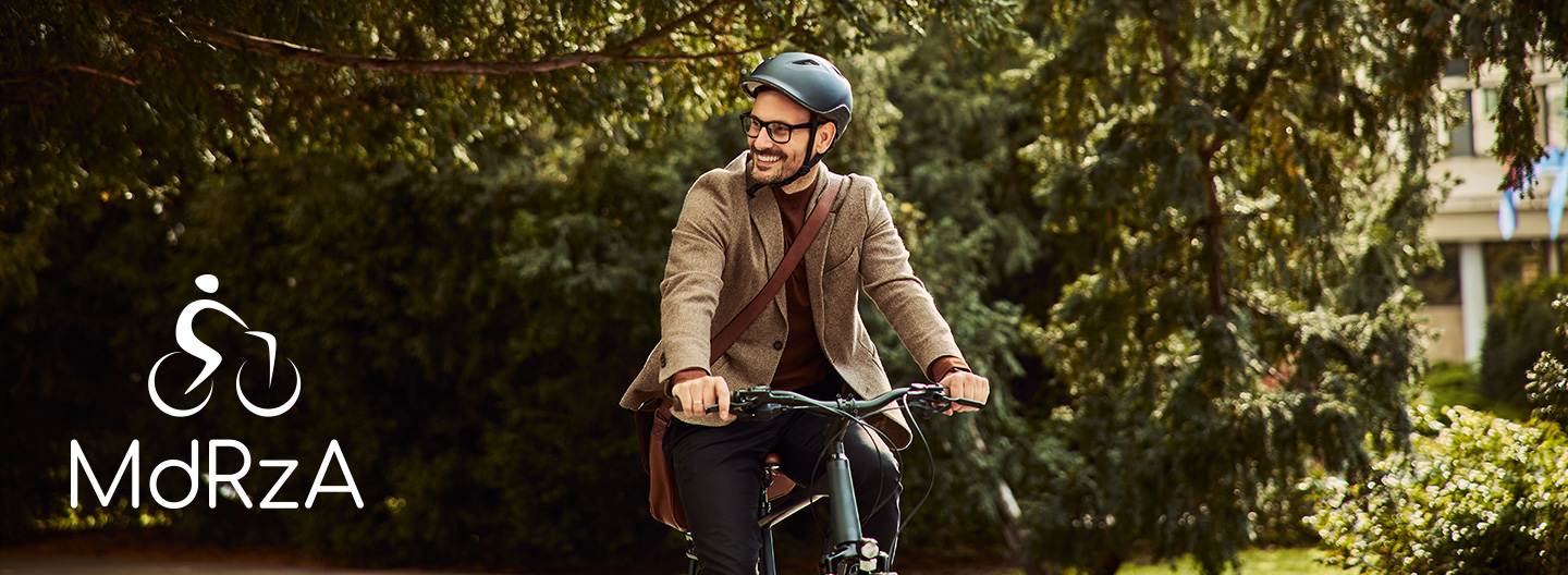 Mann mit Fahrradhelm fährt Fahrrad unter Bäumen vor einem Bürogebäude.