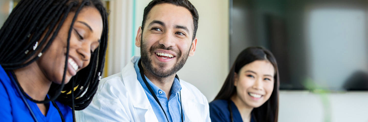 Zwei Frauen und ein Mann sprechen im medizinischen Umfeld lächelnd miteinander.