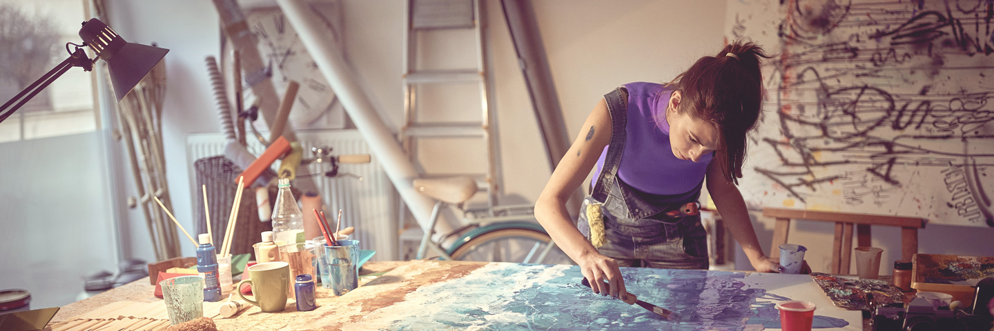Künstlersozialabgabe: Künstlerin im Atelier trägt Farbe auf eine Leinwand auf Künstlersozialabgabe: Künstlerin im Atelier trägt Farbe auf eine Leinwand auf