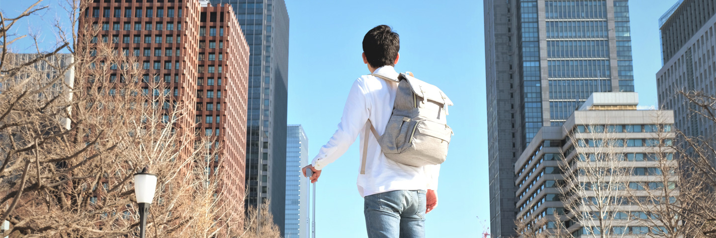 Mann mit Koffer vor Hochhäusern: Entsendungen ins Ausland in der Sozialversicherung