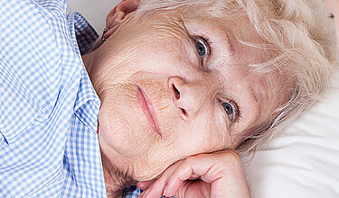 Ältere Frau, die im Bett liegt, schaut freundlich eine Krankenschwester an
