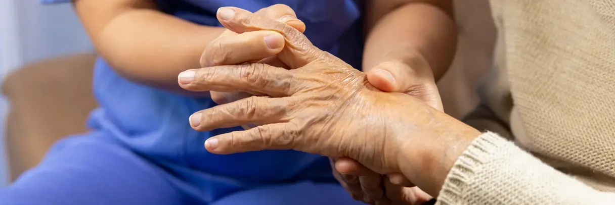 Eine Pflegekraft untersucht die Hand einer älteren Person – Fokus auf geschwollene Finger und Gelenke, möglicherweise durch rheumatoide Arthritis verursacht.