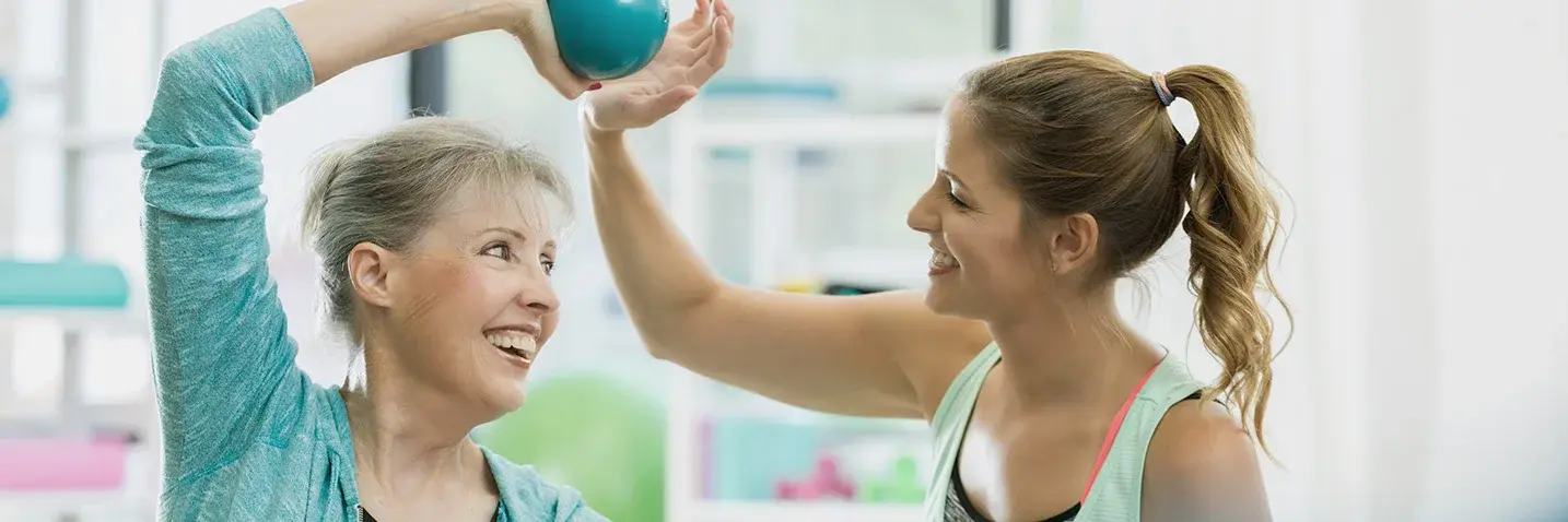 Eine Frau, die einen Ball über dem Kopf hält, lächelt eine andere Frau an