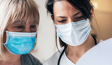 Zwei Frauen mit Mundschutz schauen auf ein Papier