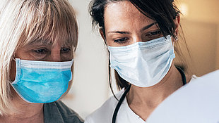 Zwei Frauen mit Mundschutz schauen auf ein Papier
