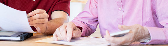 Junger Mann, der an einem Tisch sitzt, hilft Senioren beim Ausfüllen von Dokumenten