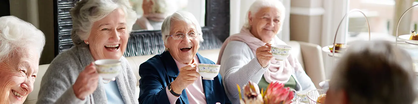 Mehrere ältere Damen sitzen am Tisch. Lachend halten die eine Tasse hoch