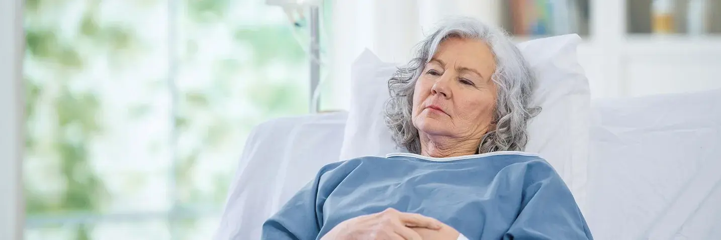 Eine ältere Frau mit grauen Haaren liegt in einem Krankenhausbett
