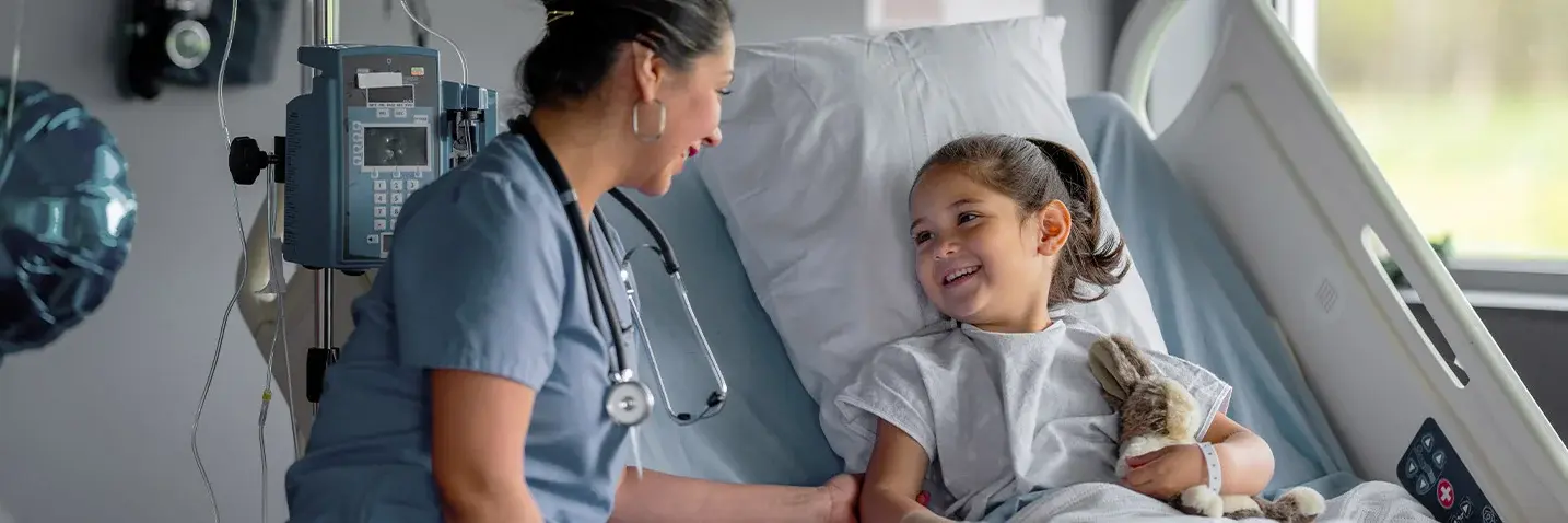 Rechts im Bild ist ein Kind auf einem Krankenhausbett. Links von ihr ist eine Ärztin zu sehen.