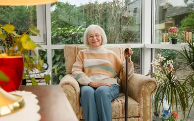 Pflegeheim: Eine Seniorin sitzt lächelnd in einem Sessel.
