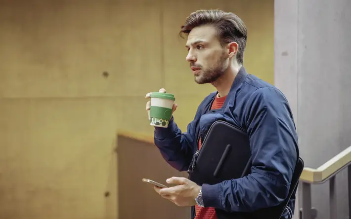 Das Bild zeigt einen jungen Mann mit Kaffeebecher und Smartphone.