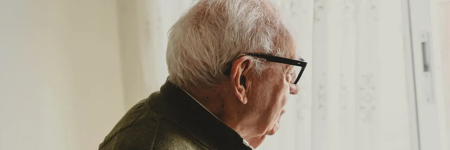 Älterer Mann mit Brille blickt aus einem Fenster.