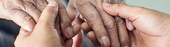 Älter Person und jüngere Person sitzen sich gegenüber und halten ihre Hände