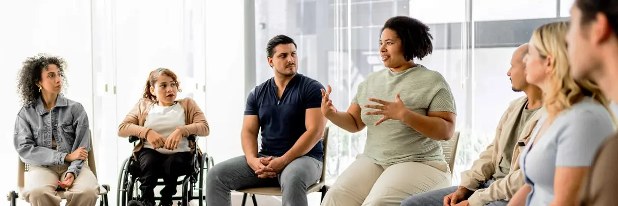 Patientenschulung in einer Gruppe: Mehrere Menschen sitzen im Kreis und hören einer sprechenden Teilnehmerin zu.