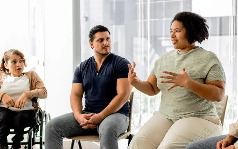 Patientenschulung in einer Gruppe: Mehrere Menschen sitzen im Kreis und hören einer sprechenden Teilnehmerin zu.