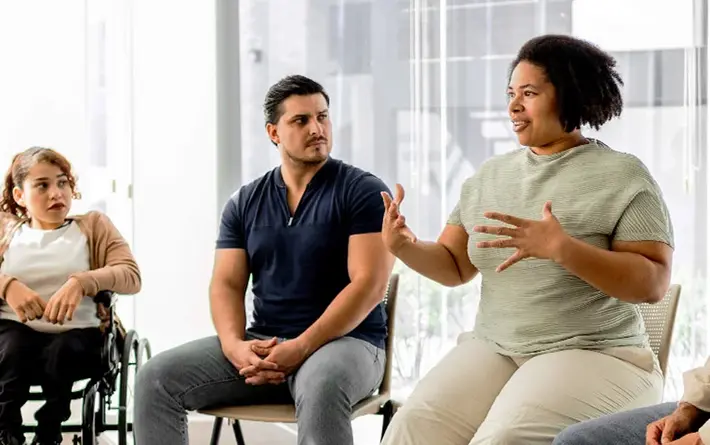 Patientenschulung in einer Gruppe: Mehrere Menschen sitzen im Kreis und hören einer sprechenden Teilnehmerin zu.
