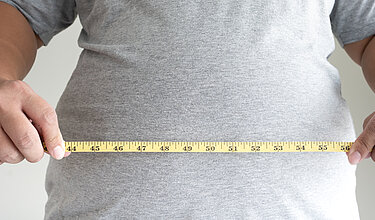 Mann hält sich ein Maßband an seinen Bauch: Symbolbild für Übergewicht