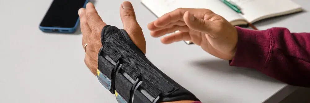 Mann mit Orthese an linker Hand legt beide Hände auf den Tisch
