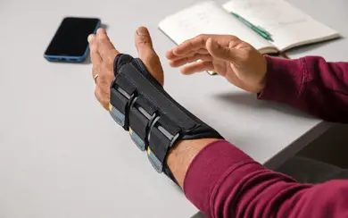 Mann mit Orthese an linker Hand legt beide Hände auf den Tisch