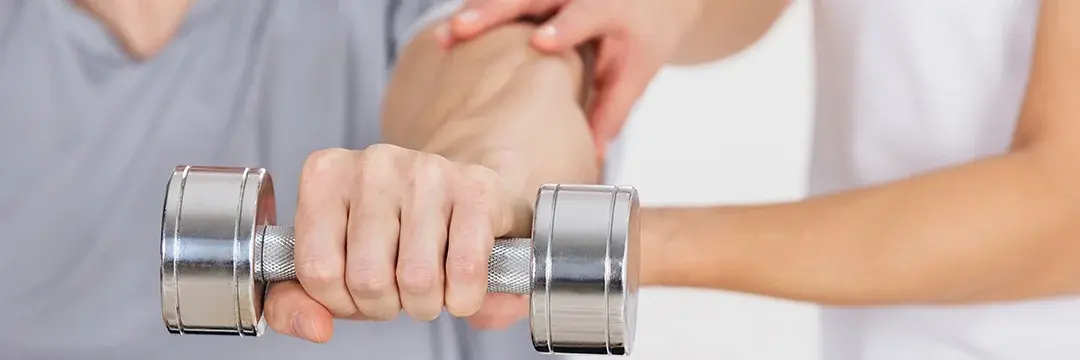 Therapeutin hilft jungen Mann bei Übungen, dieser streckt gerade ein Hantelt mit dem linken Arm nach vorn