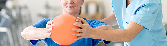 Therapeut hilft Frau bei einer Übung mit einem Ball