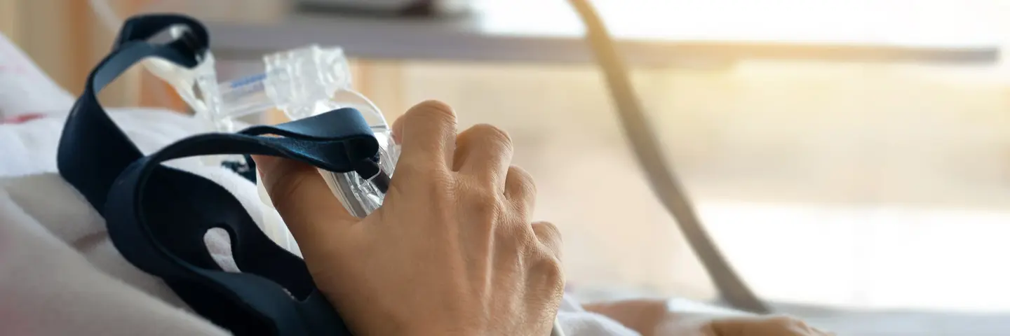 Nahaufnahme einer älteren Patientin, die durch eine Beatmungsmaske atmet. 