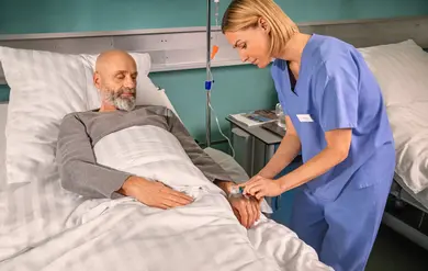 Eine Pflegerin legt einem Patienten im Krankenhaus einen Zugang an der Hand.