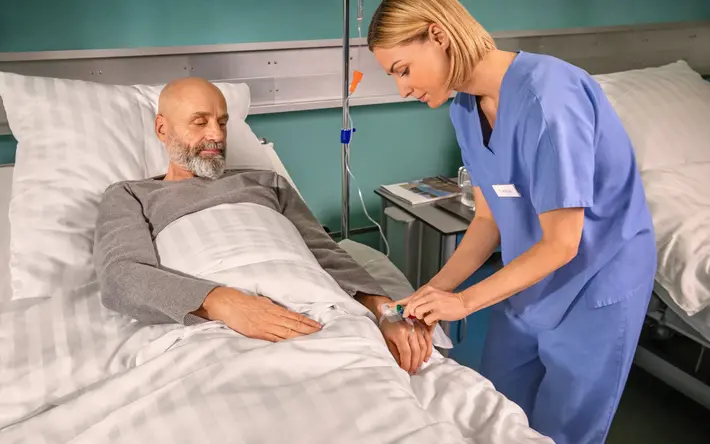 Eine Pflegerin legt einem Patienten im Krankenhaus einen Zugang an der Hand.