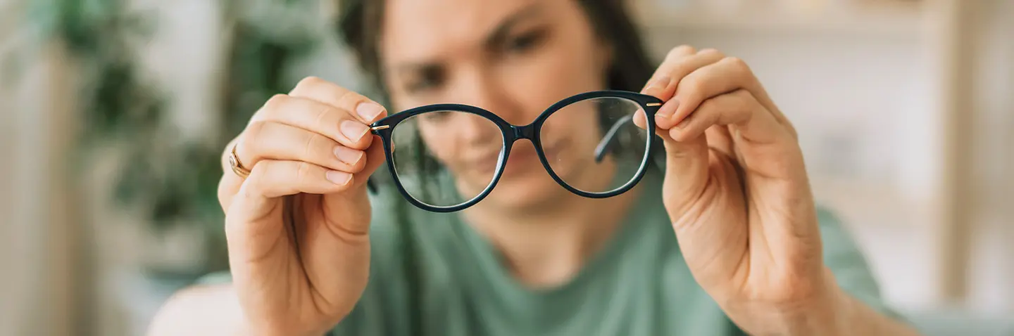 Frau hält Brille in beiden Händen, Brille und Hände scharf im Vordergrund