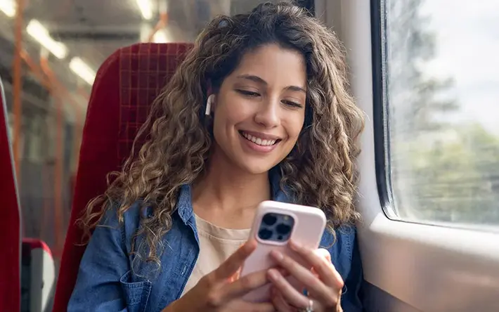 Junge Frau hört Podcast Das Bild zeigt eine junge Frau, die bei der Fahrt in einem Zug einen Podcast über ihr Smartphone hört.