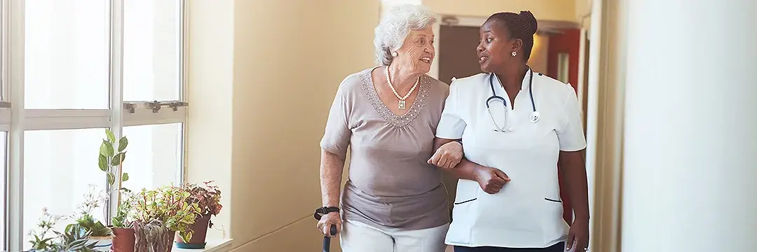 Pflegerin hilft älterer Dame beim Gehen