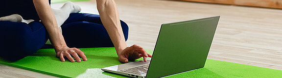 Frau sitzt auf einer grünen Trainingsmatte und schaut in den Laptop für die Videobehandlung