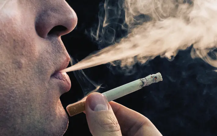 Das Bild zeigt das Gesicht eines Mannes mittleren Alters, der eine Zigarette raucht.