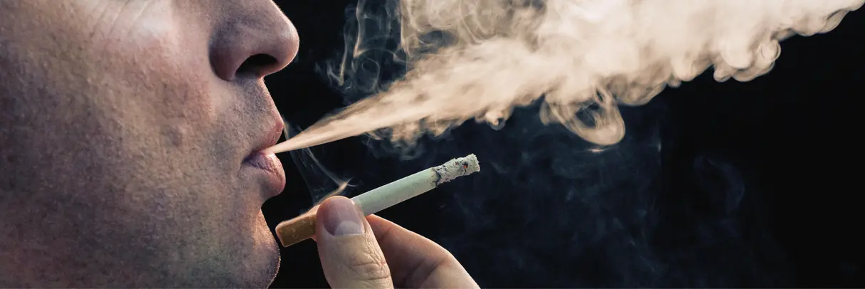 Gesundheitsrisiko Rauchen Das Bild zeigt das Gesicht eines Mannes mittleren Alters, der eine Zigarette raucht.