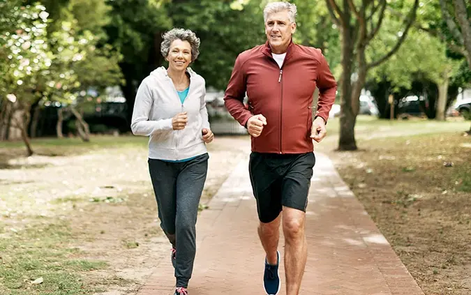 Älteres Paar joggt gemeinsam in einem Park auf einem gepflasterten Weg.