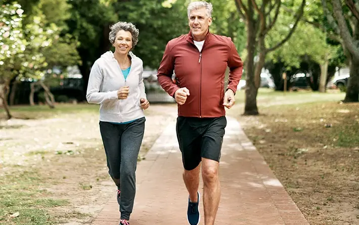 Älteres Paar joggt gemeinsam in einem Park auf einem gepflasterten Weg.