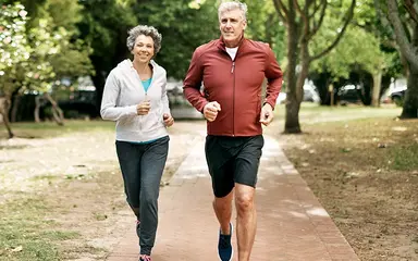Älteres Paar joggt gemeinsam in einem Park auf einem gepflasterten Weg.