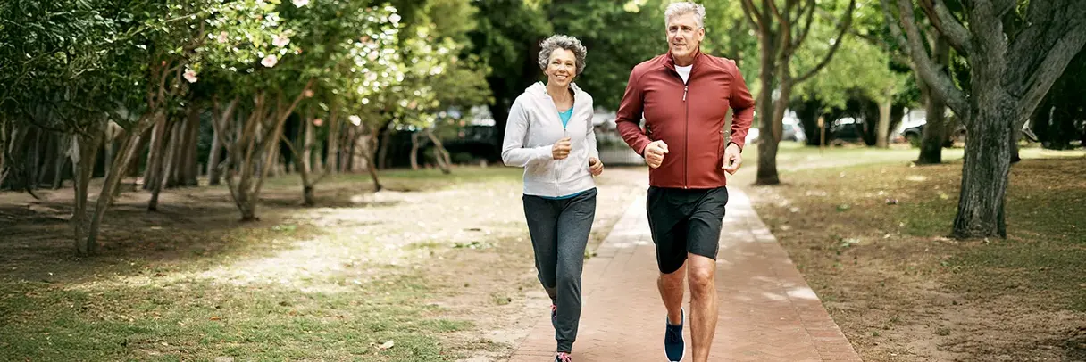 Älteres Paar joggt gemeinsam Älteres Paar joggt gemeinsam in einem Park auf einem gepflasterten Weg.