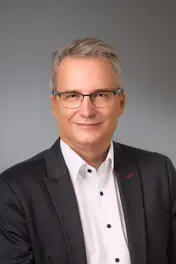 Internist Andreas Lipécz Internist Andreas Lipécz mit grauem Sakko, weißem Hemd und Brille vor grauem Hintergrund