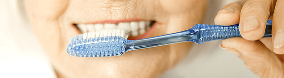 Ältere Frau hält eine Zahnbürste vor ihrem Mund und putzt Zähne
