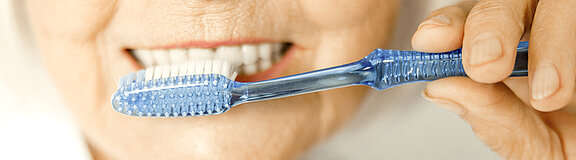 Ältere Frau hält eine Zahnbürste vor ihrem Mund und putzt Zähne