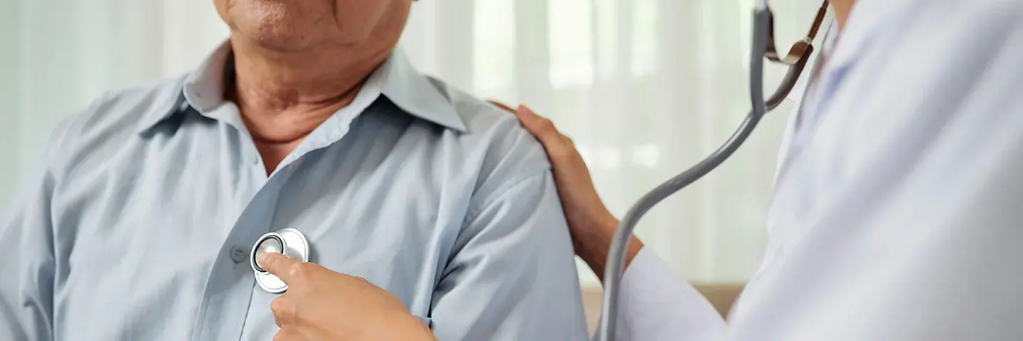 Ärztin hört bei einem älteren Patienten Herz und Lunge mit einem Stethoskop ab.