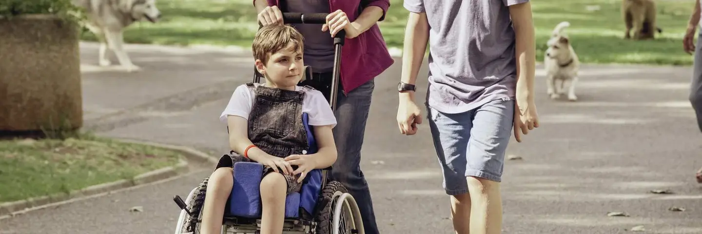 Junge Menschen schieben einen Jungen im Kinderrollstuhl durch den Park