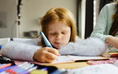 Ein Mädchen im Grundschulalter schreibt etwas in ein Heft.